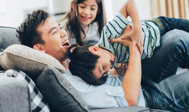 father plays on a couch with his young children